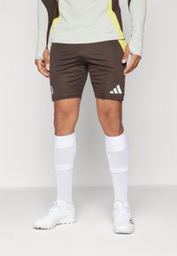Shorts de sport marron avec un logo adidas blanc et des accents jaunes, associés à des chaussettes blanches montantes et des chaussures de sport blanches.