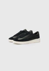 Black sneakers made of suede and leather, featuring a streamlined design, flat laces, and a contrasting white rubber sole.