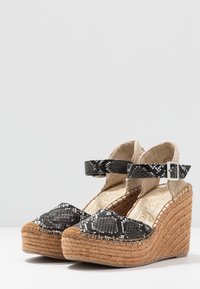 Černobílé klínové sandály s hadím vzorem, opleteným juty podpatkem, páskem kolem kotníku a texturovaným béžovým látkovým detailem. Odolný a módní design.
