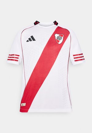 Bílý sportovní dres s krátkým rukávem, který má diagonální červený pruh, černé detaily a logo na levé části hrudi, vyrobený z prodyšného materiálu.