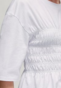 Witte T-shirt met korte mouwen, voorzien van ingezamelde elastische details bij de taille, wat zorgt voor een textuurdesign en een ontspannen silhouet.