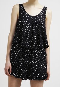 Combinaison noire à pois avec un design superposé, présentant un haut sans manches, une coupe décontractée et une taille élastique.