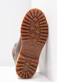 Semelle d'une botte Timberland marron avec des crampons profonds et un logo distinctif sur une surface blanche.