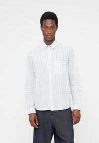 Ανοιχτό μπλε πουκάμισο με μακριά μανίκια και κάθετες ρίγες, με κουμπιά μπροστά και μία τσέπη στο στήθος· κατασ κευασμένο από υφή υφάσματος.