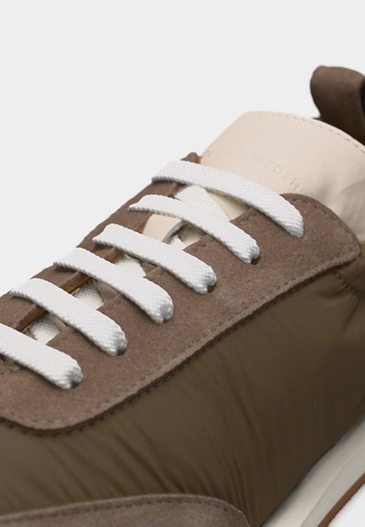 Καφέ και μπεζ αθλητικό παπούτσι με λευκά κορδόνια, πάνελ από σουέντ και ύφασμα, εμφανιζόμενο σε κοντινή λήψη των εμπρόσθιων και πλαϊνών τμημάτων.