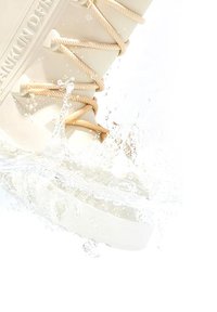 Zapato náutico impermeable beige con una superficie texturizada, que presenta cordones de cuerda color crema, parcialmente sumergido en agua con salpicaduras.