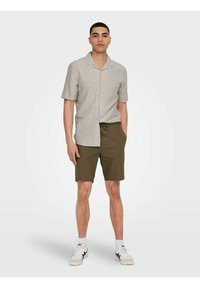 Hellgraues kurzärmliges Hemd mit Kragen, kombiniert mit olivgrünen Shorts. Das Outfit wird mit weißen Sneakern mit schwarzen Akzenten abgerundet.