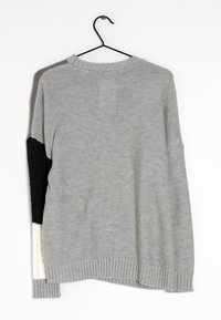 Pull en maille grise avec encolure ronde et ourlet côtelé. Présente des accents texturés et des blocs de couleur en noir et crème sur les manches.