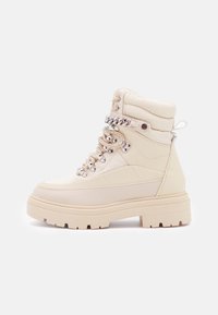 Bottes à la cheville beiges en cuir texturé avec semelle épaisse, ferrures argentées et lacets décoratifs. Col rembourré pour plus de confort.