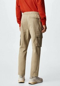 Beige cargo-broek met een elastische tailleband, zijzakken en een achterzak met rits, gecombineerd met lichtgekleurde sportschoenen.