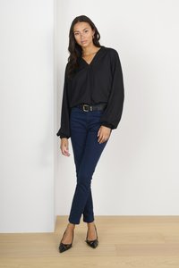 Black long-sleeve blouse with a v-neck and textured design, paired with dark blue slim-fit jeans and black pointed-toe heels.