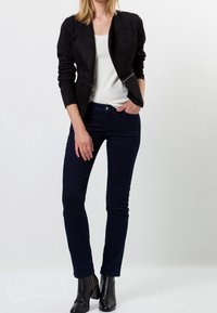 Chaqueta de ante sintético negra con un diseño ajustado, que presenta dos bolsillos frontales con cremallera. Combinada con jeans skinny azul marino y botines negros.