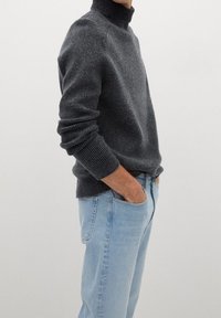 Kompakter dunkelgrauer Rollkragenpullover mit gerippten Bündchen, kombiniert mit hellblauen Jeans mit geradem Bein. Der Stoff wirkt strukturiert und warm.