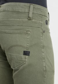 Slim-fit olivgröna jeans i denim med en svart logotyp, minimalistisk sömnad och standard bakfickor.