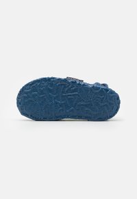Blue rubber shoe sole with textured pattern, featuring a soft felt upper and a branded tag for identification.