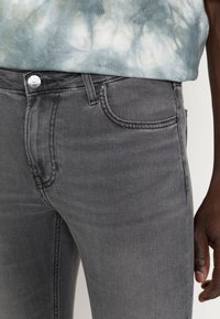 Jean en denim gris à coupe ajustée, avec une fermeture à bouton argenté, des poches avant et des détails de surpiqûres contrastées.