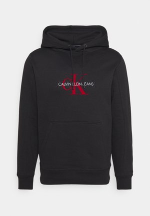 Hoodie noir en mélange de coton, avec un logo central rouge "CK" et le texte "CALVIN KLEIN JEANS", poche kangourou et poignets côtelés.