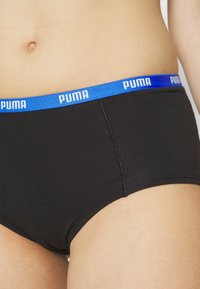 Fekete pamut alsónadrág kék gumírozott derékkal, amelyen fehér "PUMA" márkajelzés található. Az oldalsó varrások jól láthatóak.