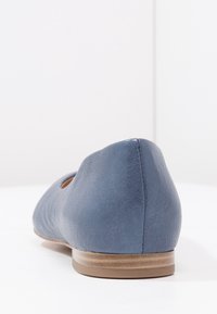 Tmavě modré kožené baleríny s kulatou špičkou a nízkým béžovým podpatkem, vyfocené ze zadu na bílém povrchu.