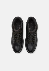 Juodos odinės kulkšninių botai su tekstūruotu pilku audiniu viduje, alyvuogių spalvos raišteliais ir šoninėmis užtrauktukais, kad būtų lengva užsidėti. Plokščios gumos padai.