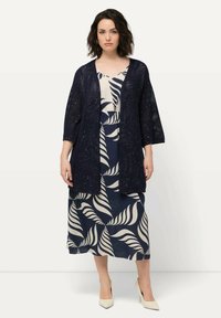 Cárdigan kimono de punto abierto en color azul marino sobre un vestido con estampado de hojas en azul marino y crema, con mangas cortas y un corte holgado. Tacones de color crema.