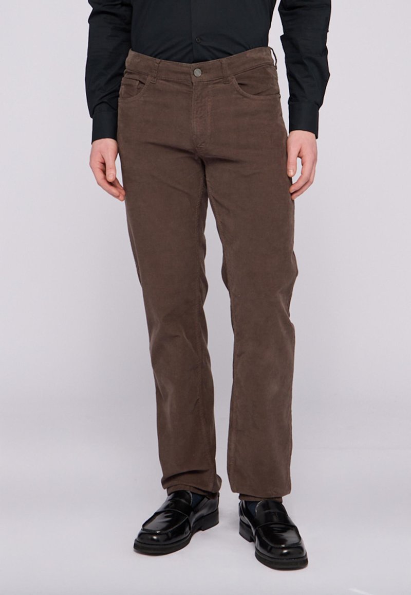 Hnědé kordové kalhoty s rovný fit, dvě přední kapsy, zapínání na knoflík a texturovaná tkanina. Spárováno s černými botami a tmavým tričkem.