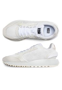 Weiße Sportschuhe aus Textil und Wildleder, mit einer runden Spitze, flachen Schnürsenkeln und einer strukturierten Sohle mit einer leichten Erhöhung an der Ferse.