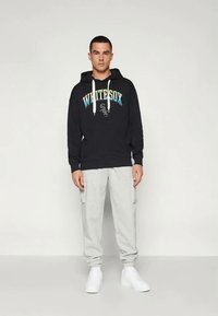 Hanorac negru cu glugă, având grafică "WHITE SOX", asortat cu pantaloni de trening gri deschis și adidași albi. Material neted, croială lejeră.