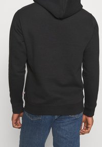 Svart hoodie i bomullsblandning, med dragsko i huvan, ribbade ärmslut och rak nederkant. Buren med blå denimjeans.