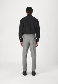 Svart långärmad skjorta med knappar, matchad med ljusgrå skräddarsydda byxor. Svarta skor fulländar outfiten.