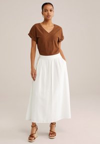 Brązowy, teksturowany top w kształcie V z krótkimi, podwiniętymi rękawami, połączony z białą, maksymalną spódnicą z eleganckim paskiem w talii i bocznymi kieszeniami. Beżowe sandały na paski.