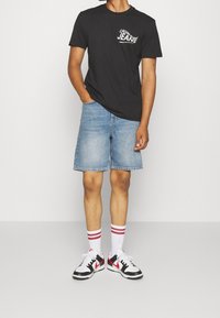 Black cotton t-shirt with white "Calvin Klein Jeans" logo, paired with blue denim shorts, white socks with red stripes, and black and white sneakers.