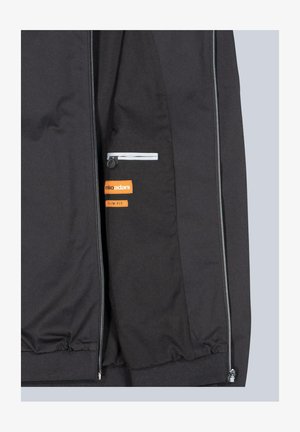 Schwarze Jacke mit tailliertem Design, ausgestattet mit einer Reißverschlusstasche, reflektierenden Akzenten und einem orangefarbenen Markenlabel. Glatte, gewebte Textur.