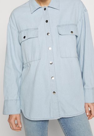 Jasnoniebieska kurtka dżinsowa z długimi rękawami, dwoma kieszeniami na piersi z klapkami i zatrzaskami oraz zapięciem na zatrzaski z przodu.