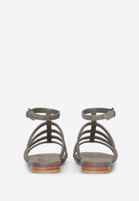 Paire de sandales plates grises avec plusieurs fines brides et fermetures à boucle à la cheville, vues de dos sur fond blanc.