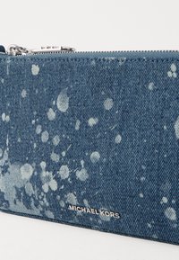 Portefeuille en denim avec un motif éclaboussé bleu et blanc, fermeture éclair et quincaillerie en argent. Présente le nom de la marque "Michael Kors" embossé sur le devant.
