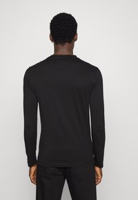 Svart långärmad skjorta i bomullsblandning med rund halsringning. Har subtila sömnadsdetaljer, åtsittande design och en mjuk textur.