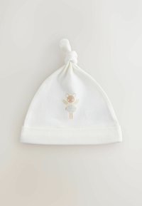Cappellino bianco per bambini lavorato a maglia con un nodo sulla sommità. Presenta un disegno stampato di un orso con ali in delicati colori pastello.