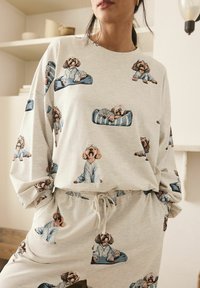 Ljusgrått lounge-set med ett upprepat hundmönster. T-shirten med lång ärm har en loose fit, medan byxorna har ett elastiskt midjeband.