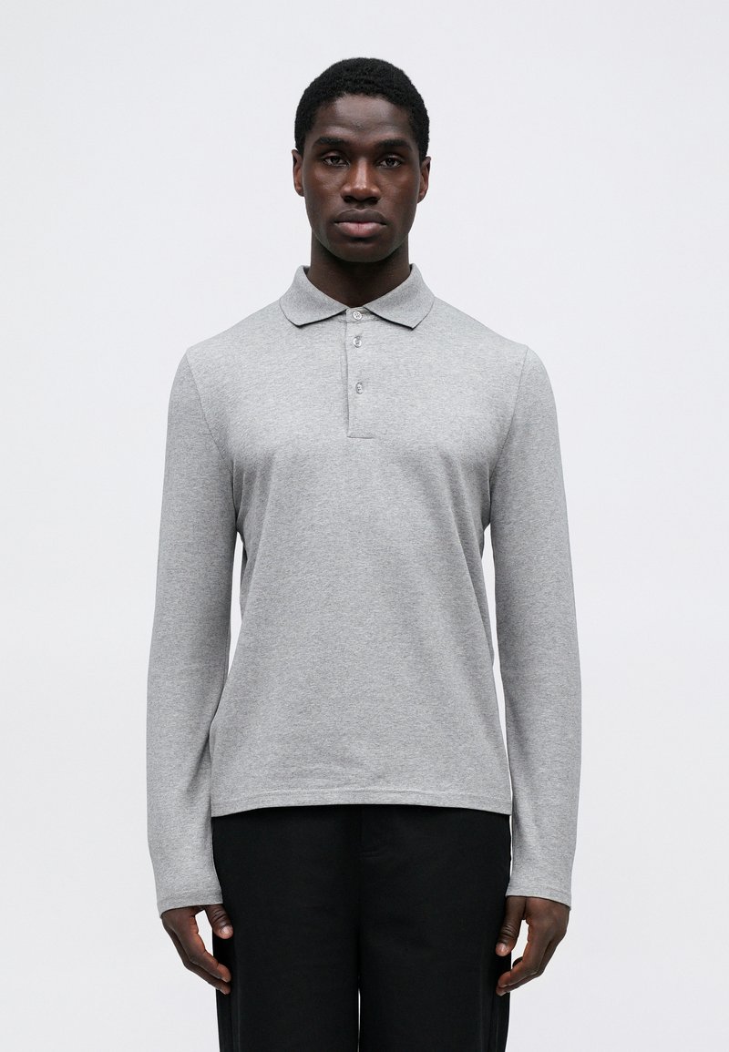 Polo shirt grigio a maniche lunghe realizzato in tessuto morbido. Presenta un colletto e una pattina con tre bottoni. Colore uniforme semplice senza motivi.