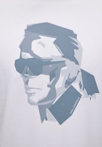 Στυλιζαρισμένο πορτρέτο σε κλίμακα του γκρι ενός άνδρα που φορά γυαλιά ηλίου και παλτό με ψηλό γιακά, με το κείμενο "Karl Lagerfeld" στον γιακά.