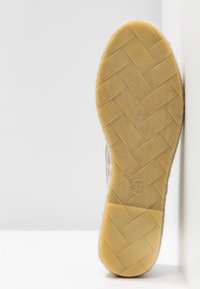 Suola di scarpa beige con un motivo testurizzato, caratterizzata da un design piatto e una marcatura circolare '37'. Il bordo mostra un dettaglio in materiale morbido.