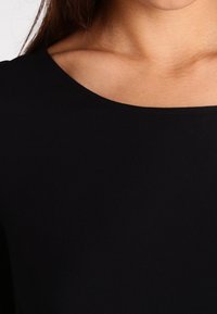 Top nero aderente con scollatura ampia e texture liscia. Il tessuto appare elastico e leggero, adatto per un abbigliamento informale.