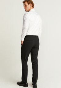 Hvid skjorte med lange ærmer parret med sorte skræddersyede bukser. Bukserne har en slim fit med baglommer. Sorte dressko fuldender looket.