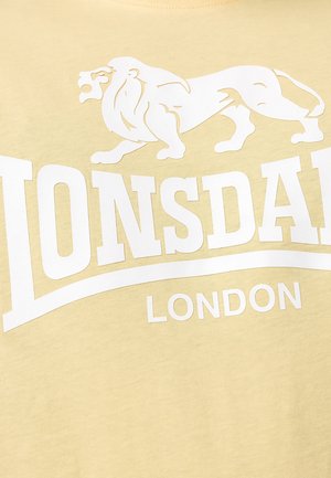 Sárga pamut póló, nagy fehér oroszlán grafikával és alatta merész "LONSDALE LONDON" felirattal. Sima tapintású, kerek nyakú kialakítás.