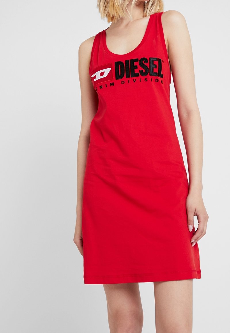 Femme portant une robe rouge sans manches avec le logo "DIESEL Denim Division" à l’avant sur un fond clair uni.