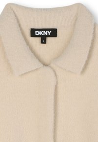 Abrigo esponjoso de color crema con cuello, que presenta una etiqueta de marca DKNY negra y una etiqueta de talla 8 en el interior del cuello.