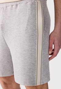 Shorts en tricot gris avec une finition texturée, des accents de rayures latérales en crème et marron foncé, et une taille élastique.