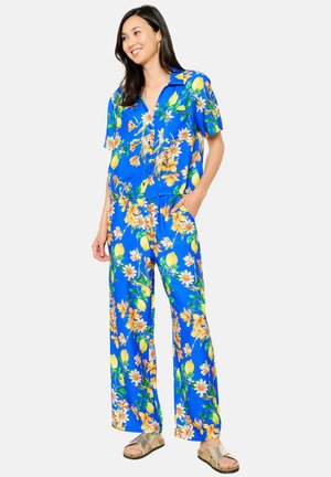 Jumpsuit floreale blu con maniche corte, colletto e gambe larghe decorate con limoni gialli e fiori arancioni.