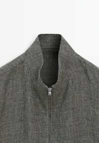 Grå, struktureret jakke med lynlås og krave i et moderne design. Har en kort krave og et diskret ternet mønster.